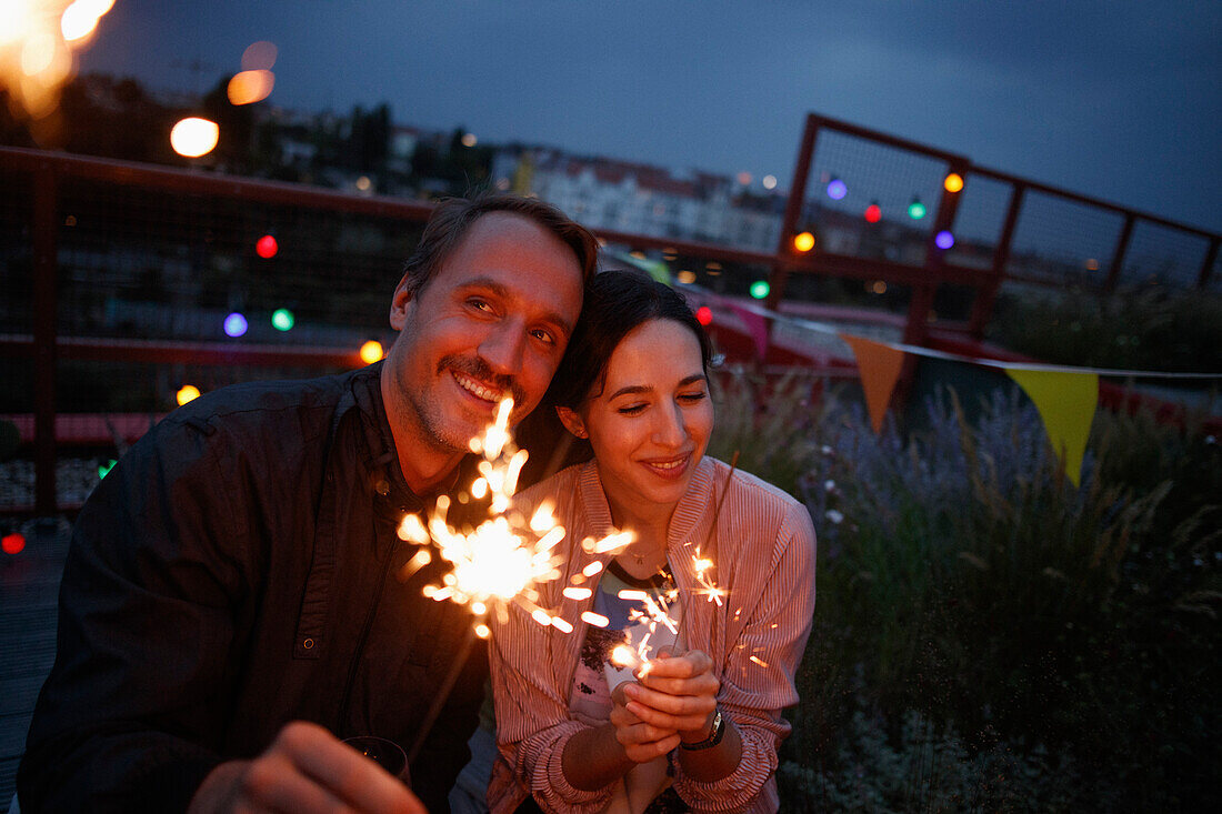 Happy couple holding sparklers on patio at night