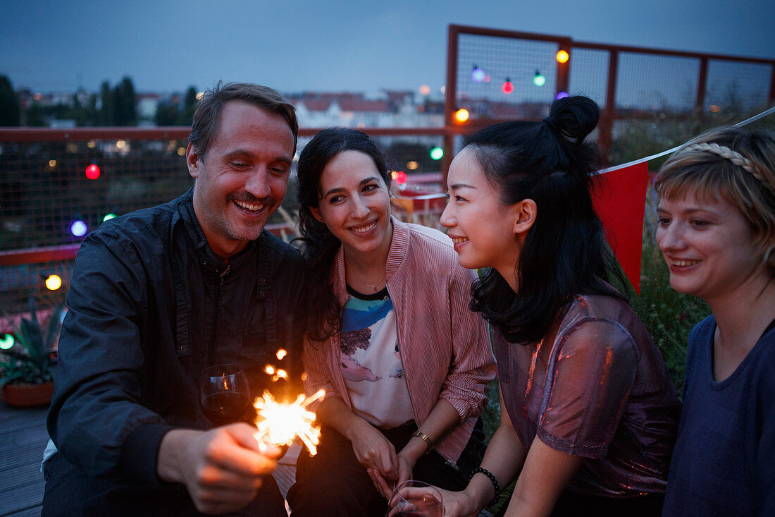 Happy man holding sparkler while sitting with female friends at night