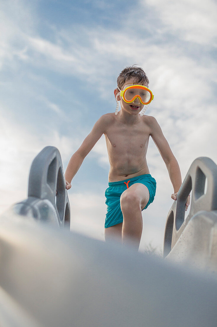 Low angle view of shirtless boy wearing swimming goggles on water slide against sky