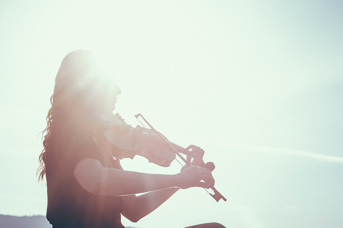 Low angle view of woman playing violin against sky on sunny day