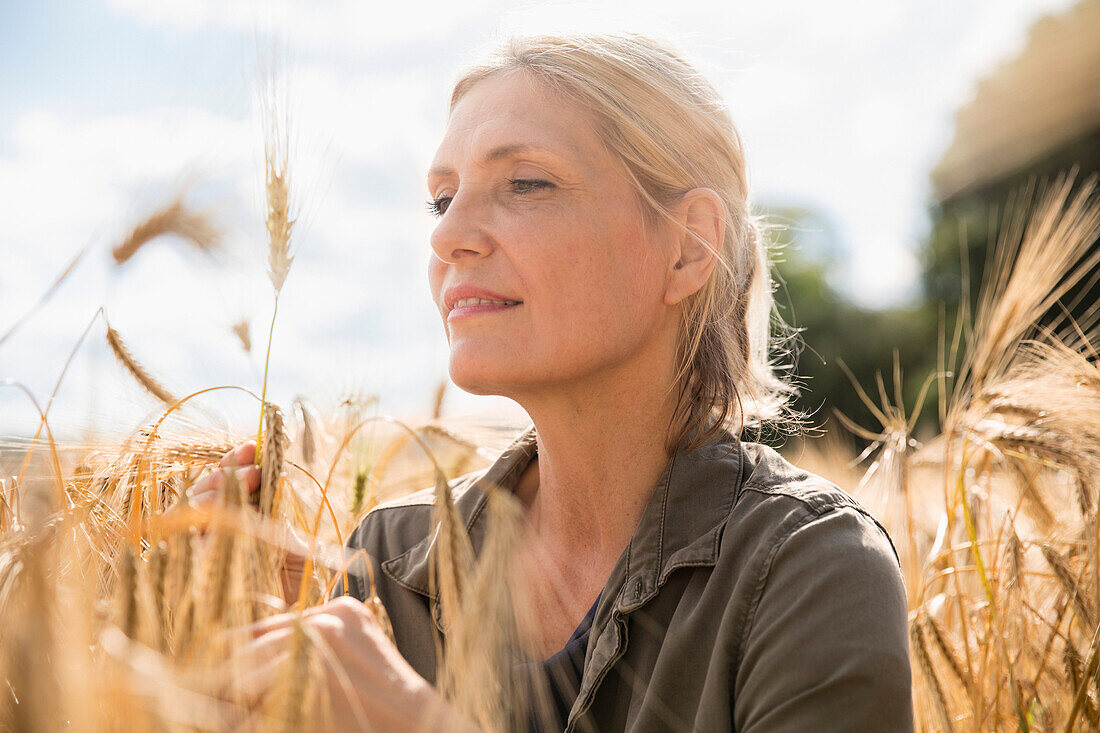 Thoughtful smiling woman looking at wheat ear in farm on sunny day