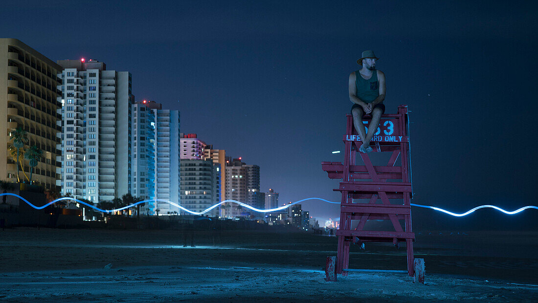 Man sitting on lifeguard chair against sky at night, Daytona, Florida, USA