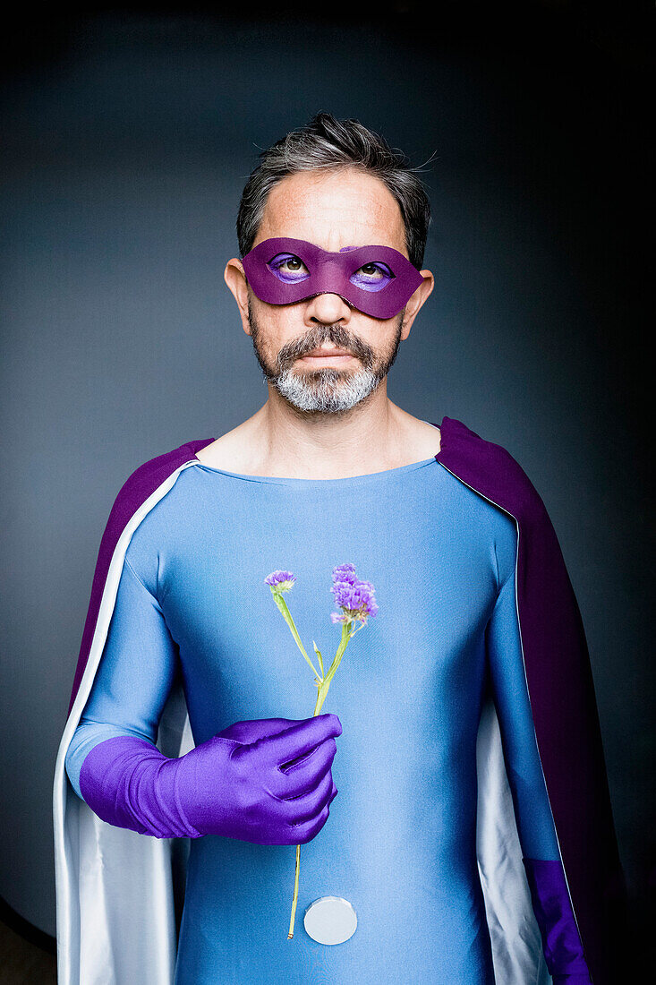 Portrait of man dressed as superhero holding flower against gray background
