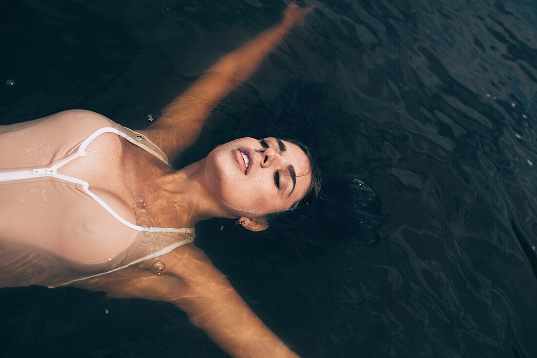 Blick von oben auf eine sinnliche junge Frau, die mit erhobenen Armen auf einem See schwimmt