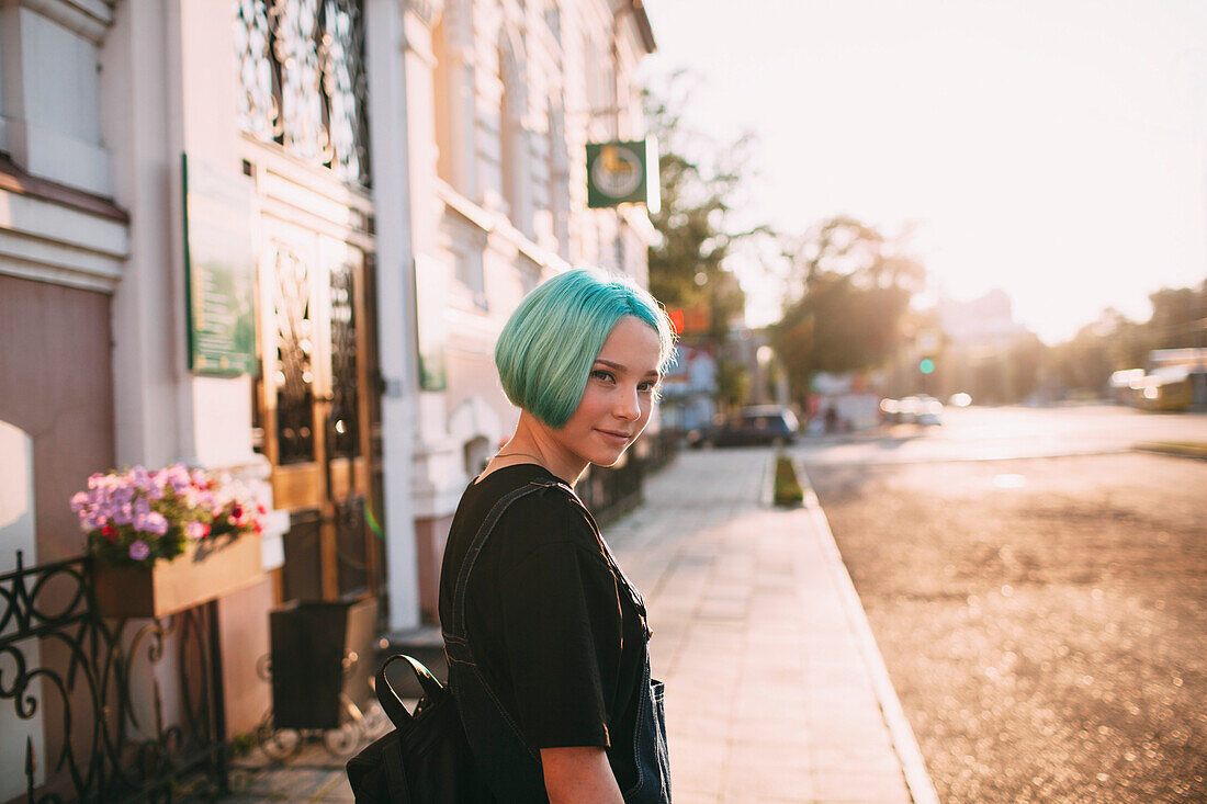 Portrait of smiling teenage girl standing on sidewalk in city during sunny day