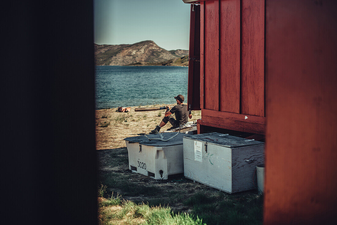 Hiker in front of a red cabin greenland, greenland, arctic.