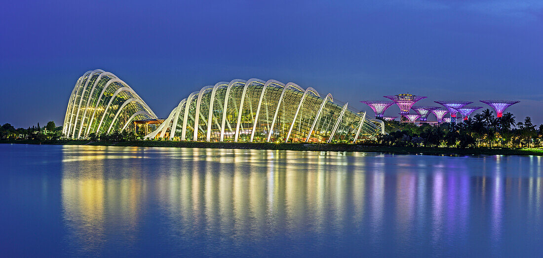 Panorama mit beleuchteter Garden of the Bay mit Cloud Forest, Flower Dome und SuperTrees spiegelt sich in Marina Bay, Singapur