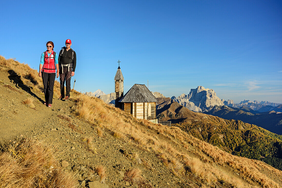 Mann und Frau wandern mit Kapelle und Monte Pelmo im Hintergrund, Col di Lana, Dolomiten, UNESCO Welterbe Dolomiten, Venetien, Italien