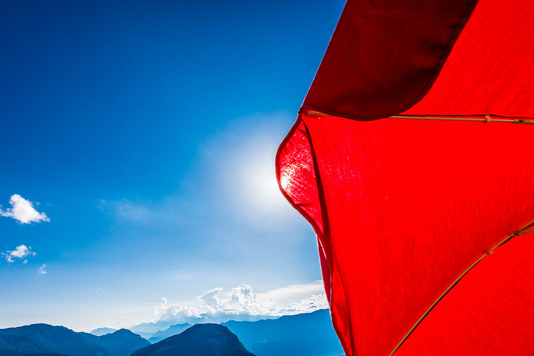 Blick an einem strahlenden Sommertag vorbei an einem roten Sonnenschirm auf das Alpenpanorama, Radein, Südtirol, Alto Adige , Italien