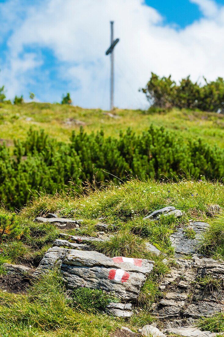 Wanderweg mit gemalten Hinweiszeichen auf einem Stein und einem Gipfelkreuz im Hintergrund, Zillertal, Tirol, Österreich