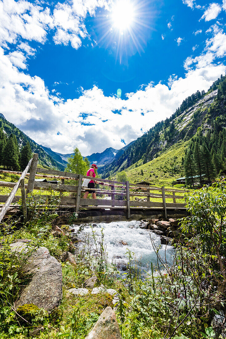 A hiker crosses a bridge with a mountain stream at the beginning of the high valley on the way to the Maxhütte, Ginzling, Zillertal, Tirol, Austria