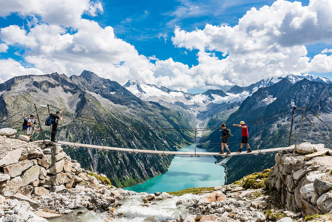 Hiker  on a suspension bridge above the mountain hut Olpererhütte in front of the panorama of the Zillertal Alps with the reservoir Schlegeisspeicher, Schlegeisspeicher, Ginzling, Zillertal, Tyrol, Austria