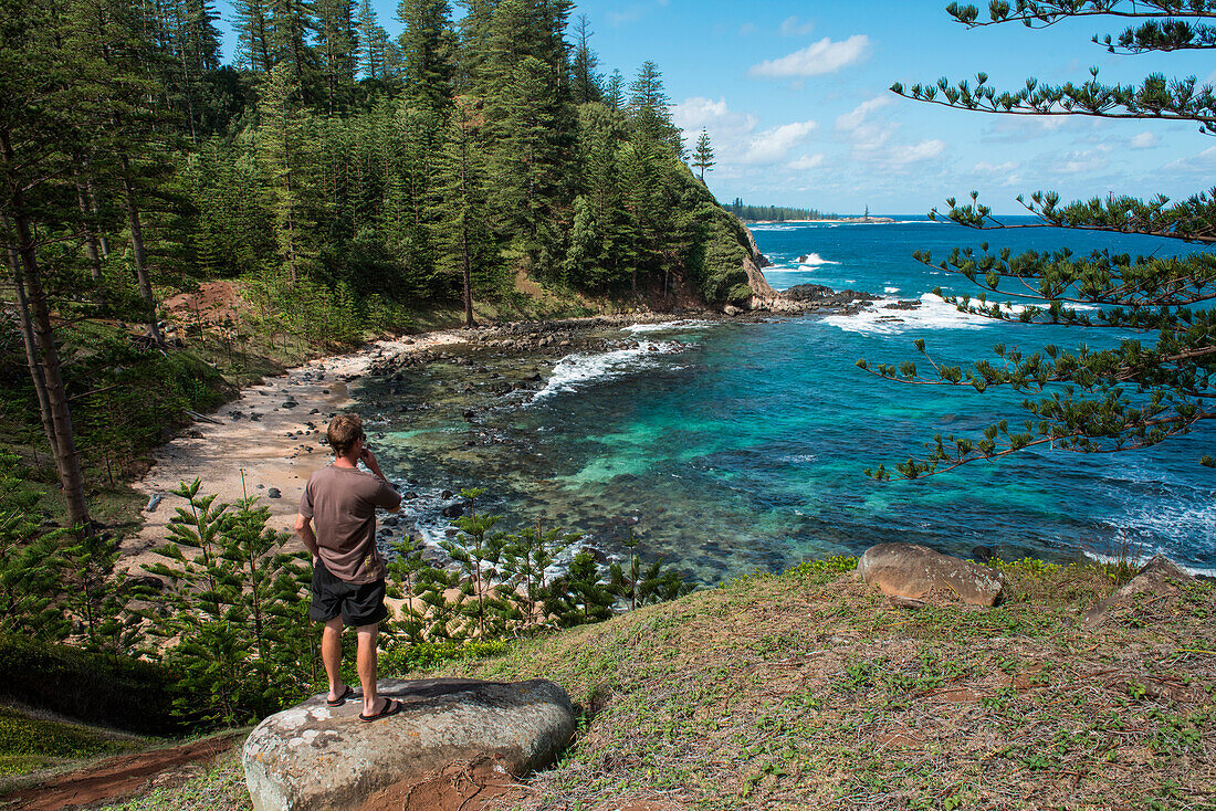 Ein junger Mann genießt eine Zigarette und die schöne Aussicht über eine der vielen beliebten Buchten, Norfolk Island, Australien