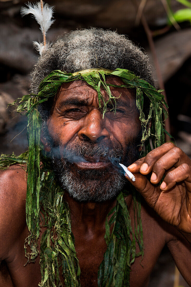 Ein einheimischer Mann mit Bart und grünem Kopfschmuck raucht eine selbstgemachte Zigarette, Waisisi Bay, Tanna Island, Vanuatu, Südpazifik