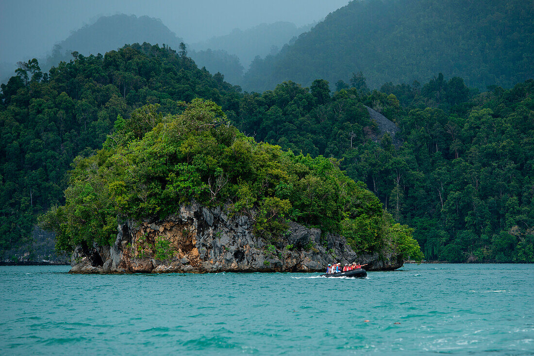 Ein Zodiac Schlauchboot mit Gästen von Expeditions-Kreuzfahrtschiff MS Bremen (Hapag-Lloyd Cruises) fährt durch eine Landschaft mit üppigen bewaldeten Hügeln, Arguni, Papua, Indonesien, Asien