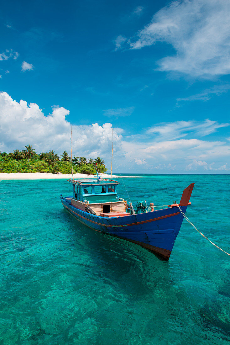 Ein buntes Boot treibt in klarem türkisfarbenen Wasser vor einer Insel, Senua, Indonesien