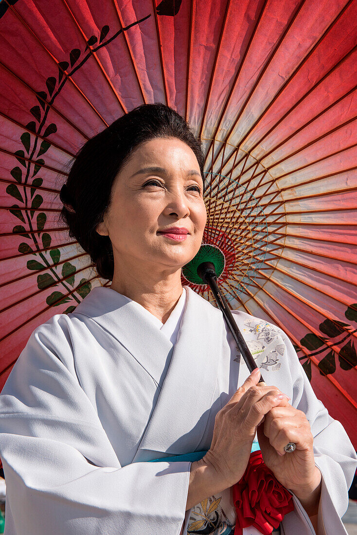 Eine Japanerin mittleren Alters, die einen Kimono trägt und einen Sonnenschirm hält, schaut in die Ferne, Kanazawa, Ishikawa, Japan, Asien