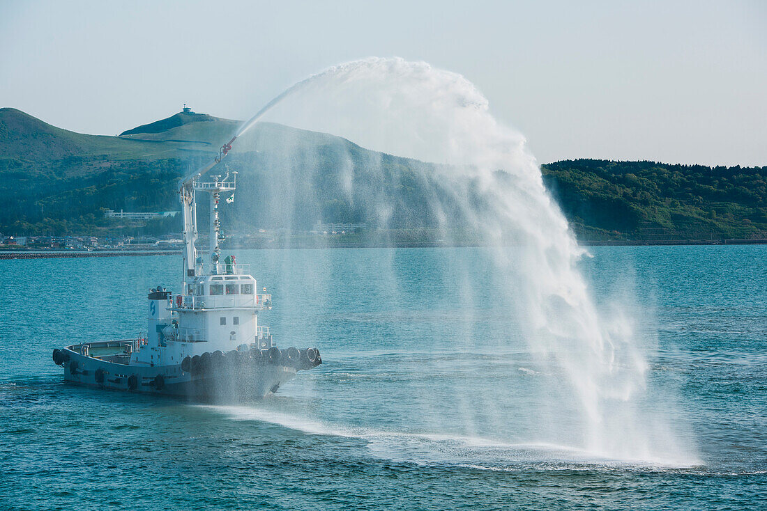 As a welcoming gesture, a tug sprays water for expedition cruise ship MS Bremen (Hapag-Lloyd Cruises), Funagawa, Oka, Akita, Japan, Asia