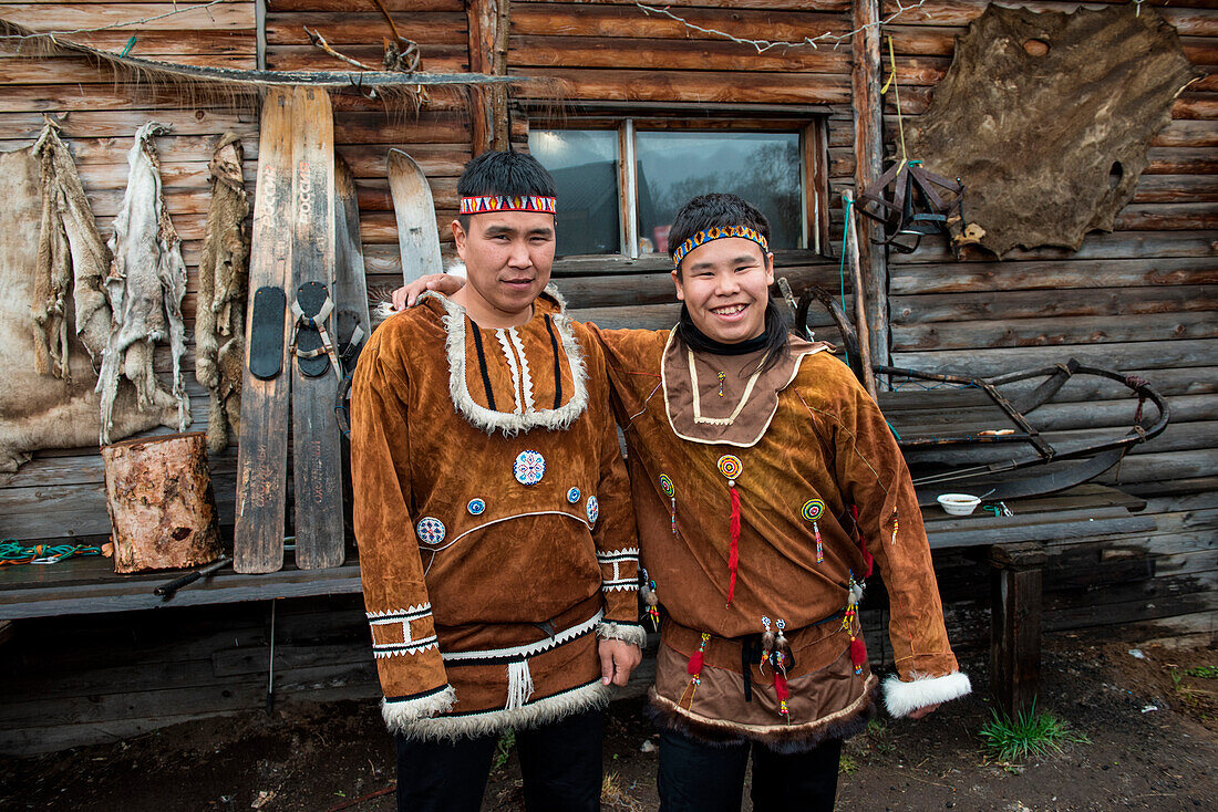 Zwei junge lächelnde Männer in traditionellem Itelmen-Kostüm stehen vor einem Privathaus, Itelmen Homestead, Kamchatka, Russland, Asien