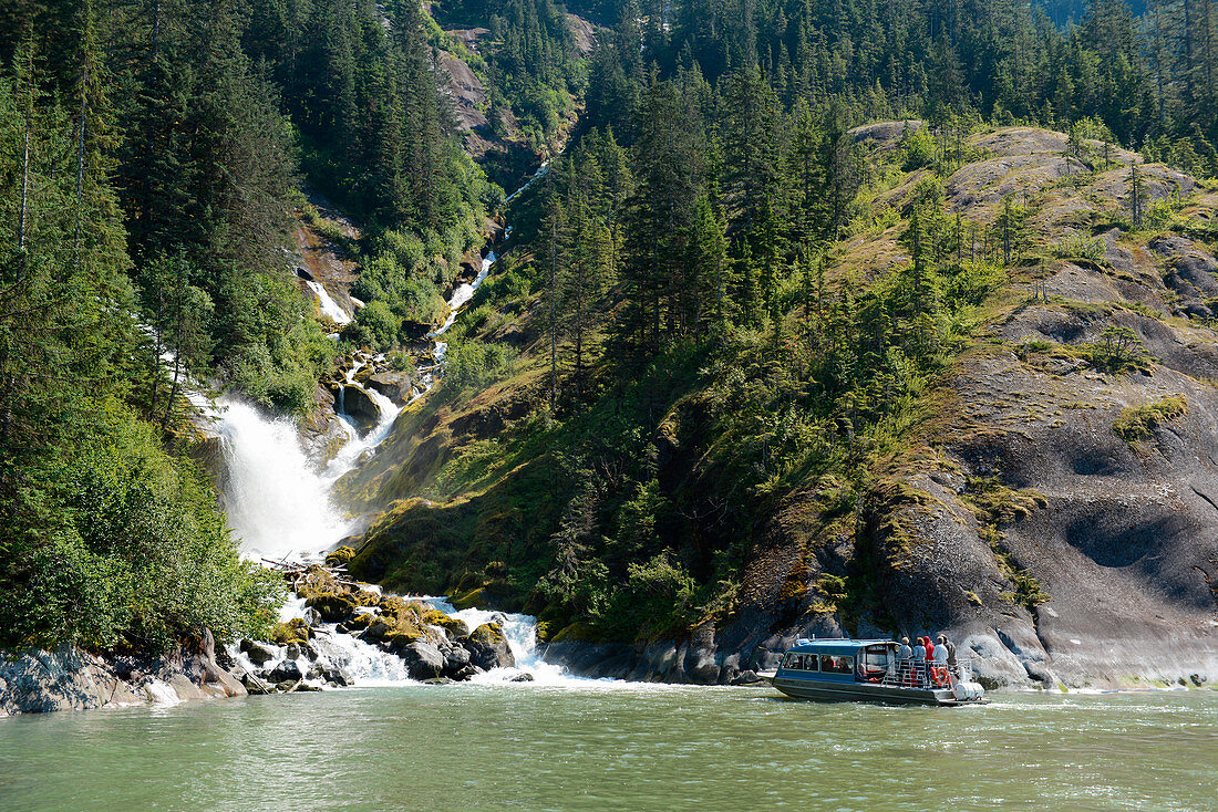 Touristen in einem Jet-Boot nähern sich einem Wasserfall umgeben von Bäumen und Büschen, LeConte Bay, Tongass National Forest, Alaska, USA, Nordamerika