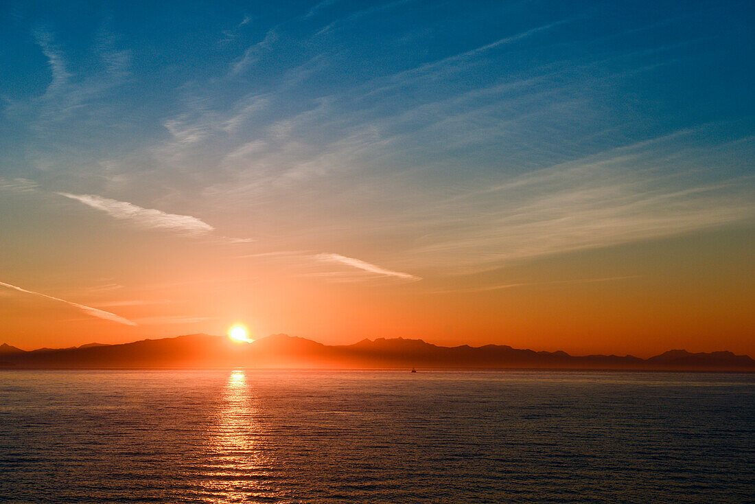 Ein einzelnes Fischerboot kehrt in seinen Hafen zurück während die Sonne über einer Bergkette untergeht, Prince Frederick Sound, Alaska, USA, Nordamerika