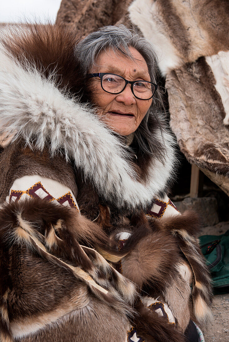 Eine ältere Frau mit Brille und traditioneller Pelzkleidung sitzt vor einem Tipi Zelt aus Rentierfell, Gjoa Haven, King William Island, Nunavut, Kanada, Nordamerika