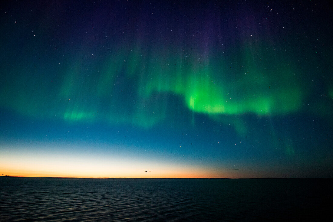 Die Nordlichter (auch Polarlichter oder Aurora Borealis) erhellen den Himmel kurz nach Sonnenuntergang, gesehen von an Bord Expeditions-Kreuzfahrtschiff MS Bremen (Hapag-Lloyd Cruises), zwischen Nordostkap und Kap Ossory, Nunavut, Nordkanada, Nordamerika