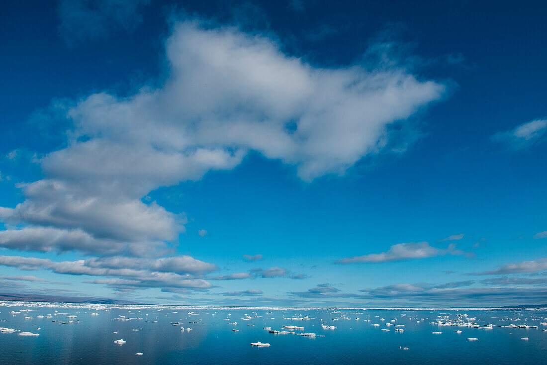 Calm waters are dotted with pieces of sea ice under a partly cloudy blue sky, seen from aboard expedition cruise ship MS Bremen (Hapag-Lloyd Cruises), Fury and Hecla Strait, Nunavut, Canada, North America