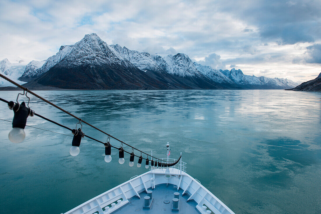 Snow-capped basalt mountains reach to the clouds over the 170 km long Søndre Strømfjord with bow of expedition cruise ship MS Bremen (Hapag-Lloyd Cruises), Søndre Strømfjord, Greenland