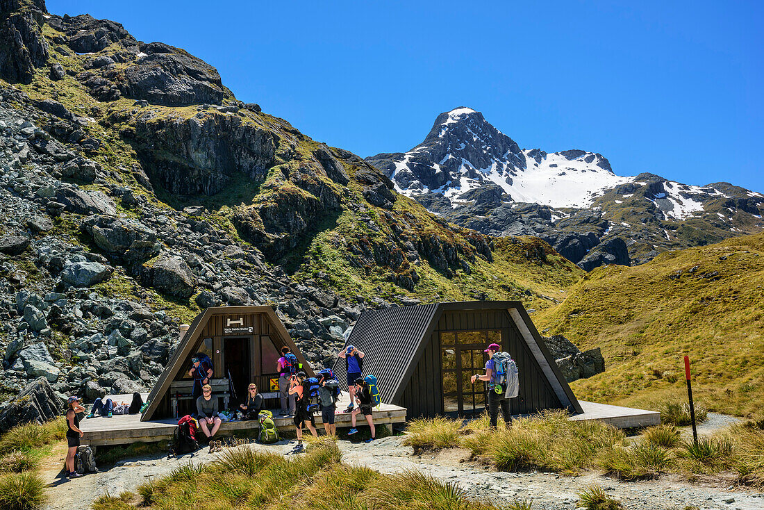 Mehrere Personen stehen vor Schutzhütten am Harris Sattel, Routeburn Track, Great Walks, Fiordlands Nationalpark, UNESCO Welterbe Te Wahipounamu, Queenstown-Lake District, Otago, Südinsel, Neuseeland