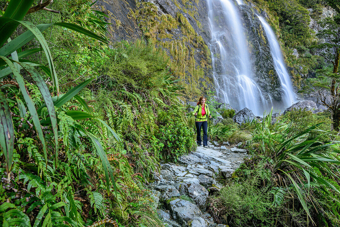 Frau wandert unter Wasserfall hindurch, Earland Falls, Routeburn Track, Great Walks, Fiordlands Nationalpark, UNESCO Welterbe Te Wahipounamu, Queenstown-Lake District, Otago, Südinsel, Neuseeland