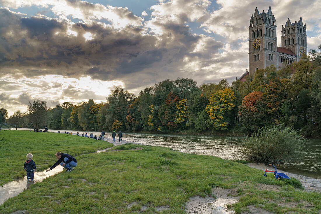 Father playing with his son on the banks of the river Isar, Church of St. Maximilian in the background, passersby standing at the autumnal banks of the river, Munich, Upper Bavaria, Germany