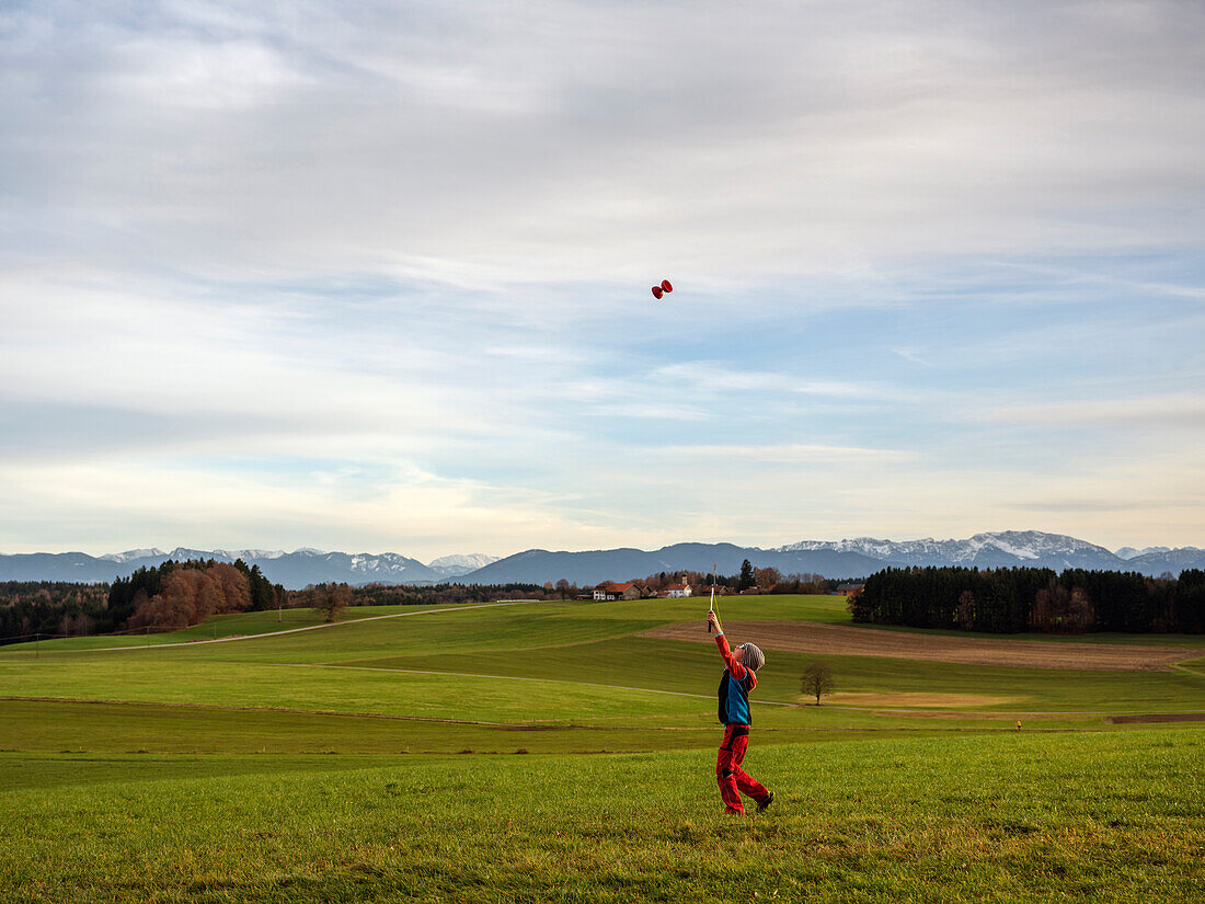 A kid playing with a „Diabolo“ on Degerndorfer Hoehe, in the back alpine peaks, Muensing, Upper Bavaria, Germany