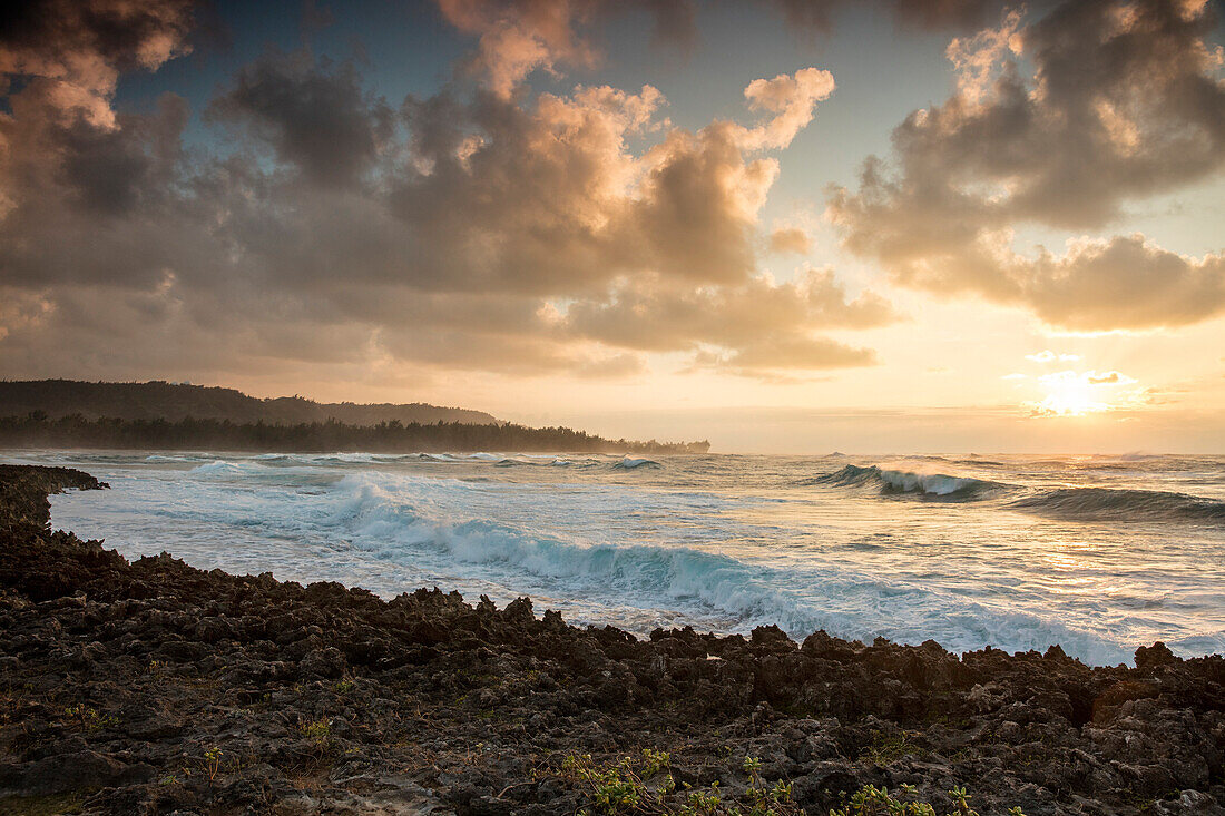 HAWAII, Oahu, North Shore, waves crashing into the rocks at Turtle Bay Resort at Sunset