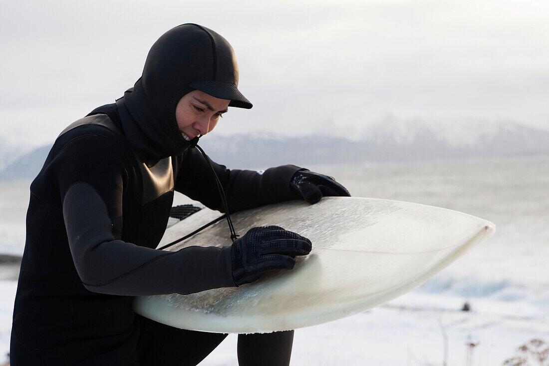 Surfer Waxing A Surfboard In Winter Along Kachemak Bay, Homer Spit, Southcentral Alaska, USA