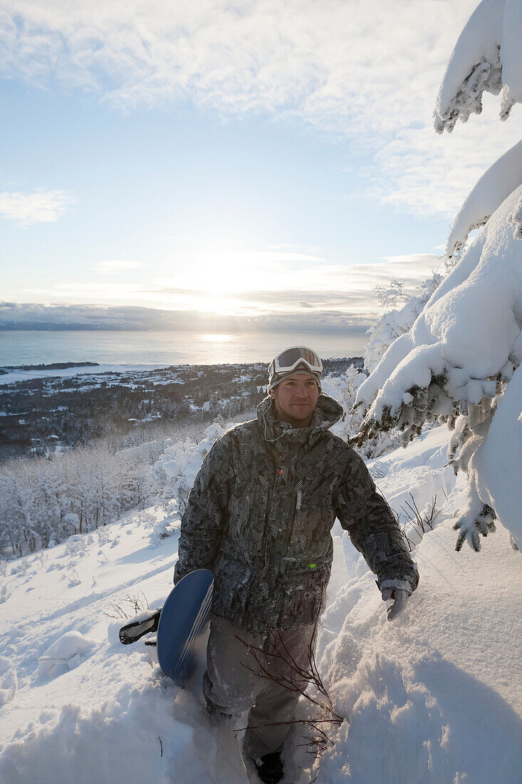 Snowboarder on a hillside overlooking Kachemak Bay at sunset, Homer, Southcentral Alaska, USA