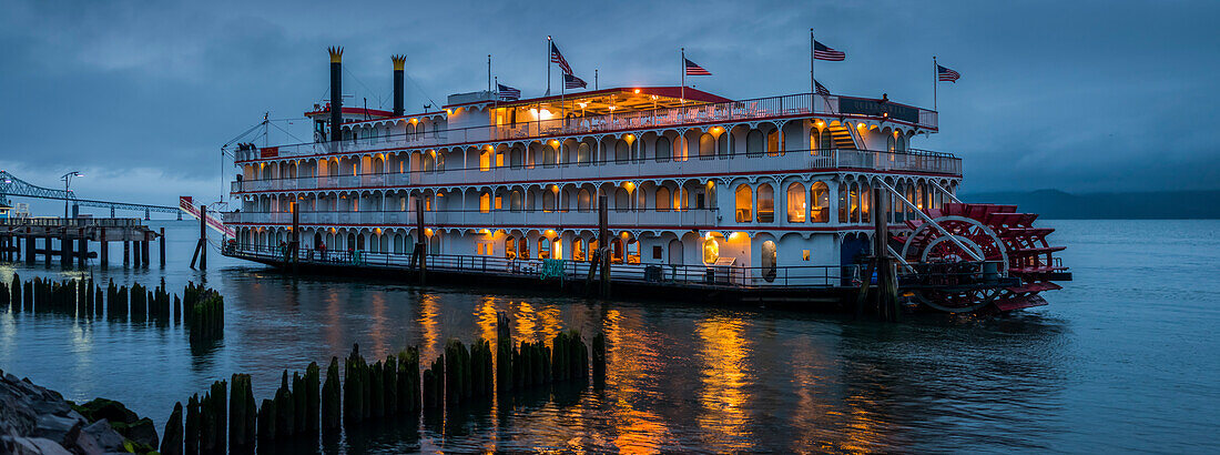 Lights illuminating a river boat docked on the Columbia River at dusk; Astoria, Oregon, United States of America