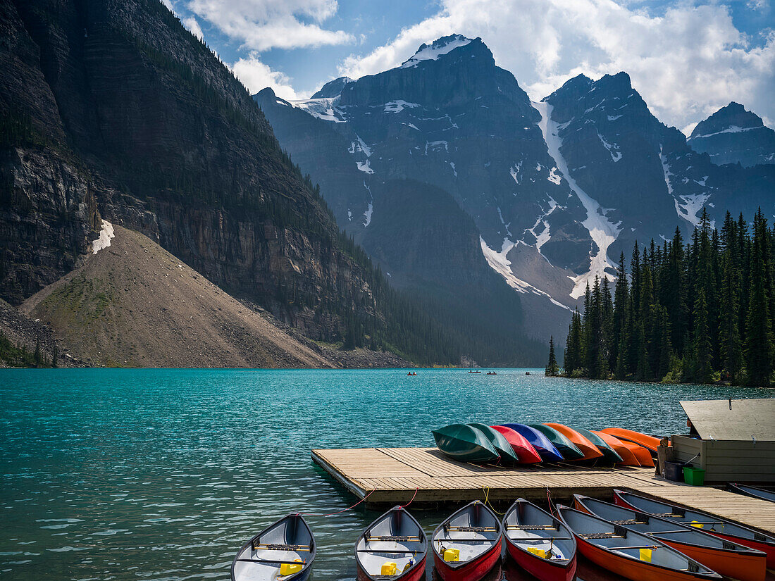 Canoes in the water and sitting on a dock along the shore of Moraine Lake in the Canadian Rocky Mountains; Eldon, Alberta, Canada