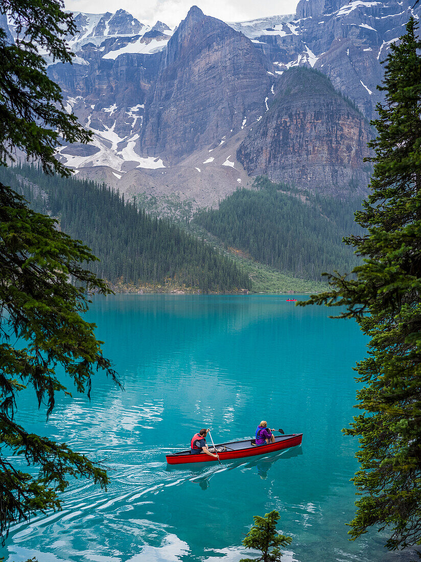 A red canoe in Moraine Lake with a cliff of the Canadian Rocky Mountains along the shoreline; Lake Louise, Alberta, Canada