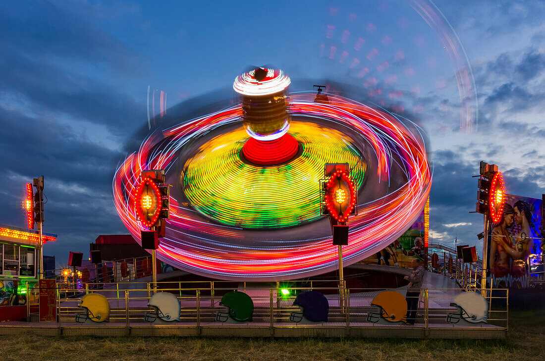 Amusement park ride glowing at dusk with colourful lights and motion blur; Newcastle Upon Tyne, Tyne and Wear, England
