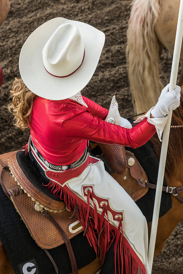High angle view of a woman wearing a white cowboy hat and riding a horse at the Calgary Stampede; Calgary, Alberta, Canada