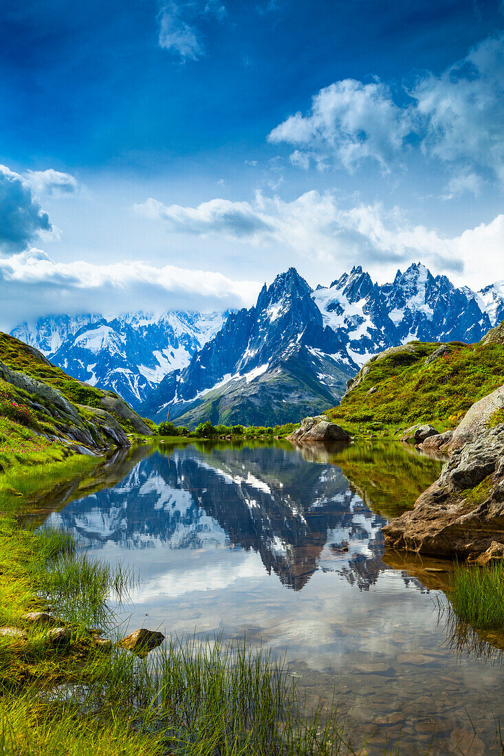 Aiguille des Charmoz, part of Aiguilles de Chamonix, reflects on Lac Flegere surrounded with green meadow, Aiguilles Rouges; Chamonix-Mont-Blanc, Haute-Savoie, France