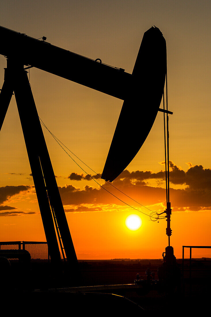 Silhouette Of A Pumpjack At Sunrise With A Colourful Orange Sun, Clouds And Sky; Alberta, Canada