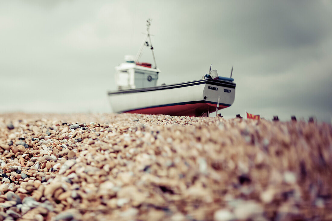 A fishing boat sits on the rocky beach under a cloudy sky; Hastings, England