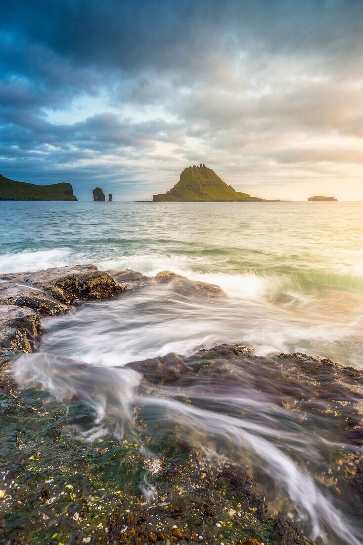 Vagar island, Faroe Islands, Denmark. Coastal rocks with Tinholmur islet at the background at sunset.