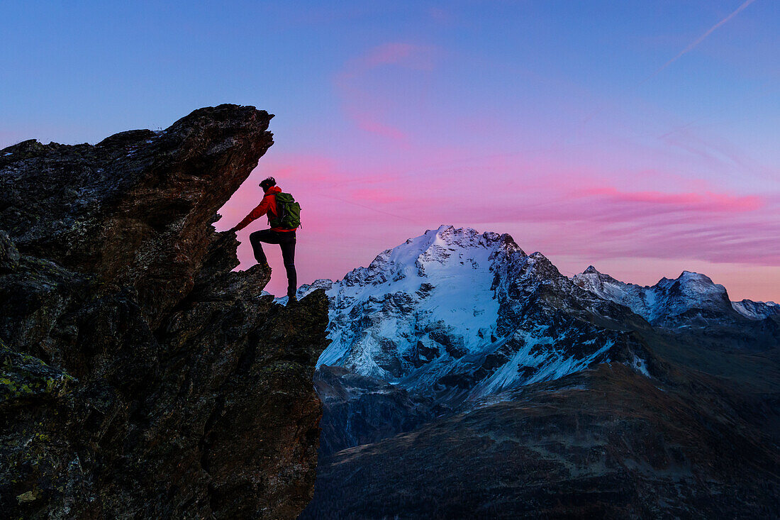 An hiker climbing a rock in Viola valley with a panoramic view at sunset. Valdidentro, Valtellina, Lombardy, Italy