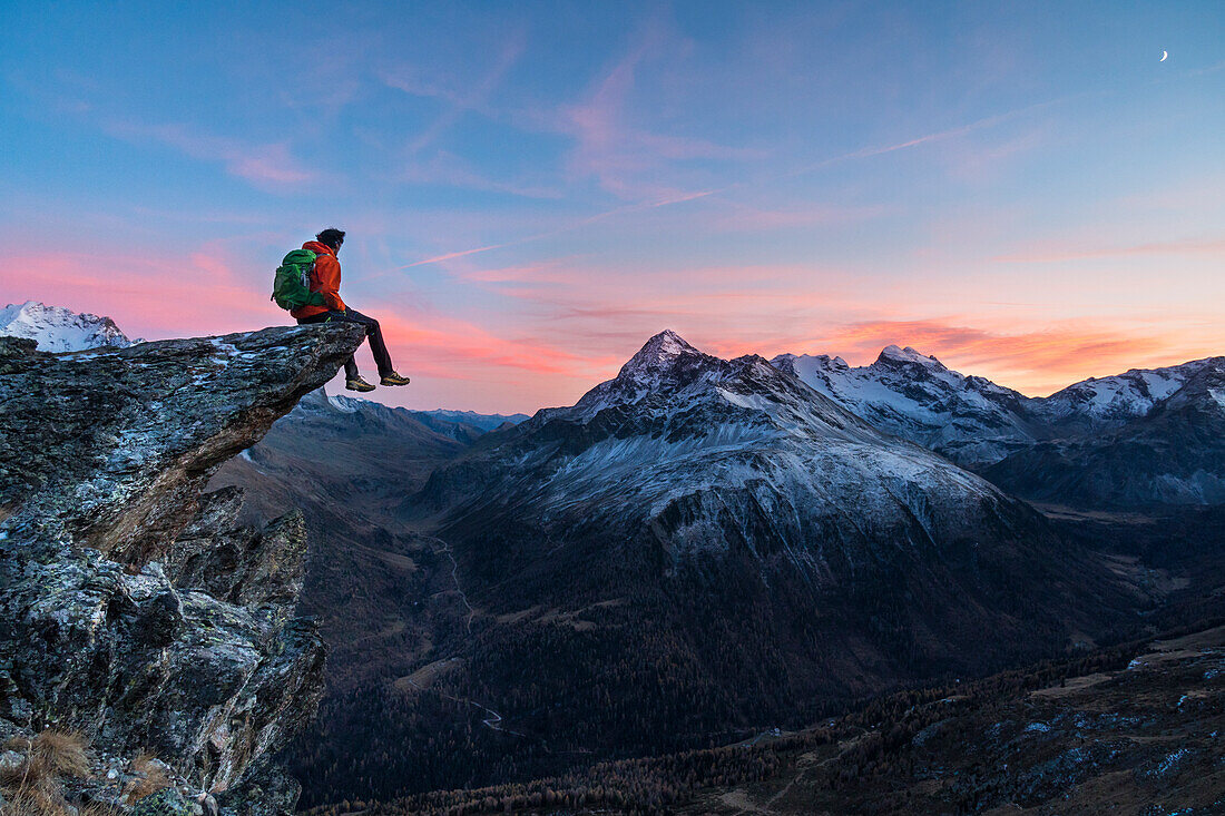 An hiker on a rock in Viola valley with a panoramic view to the Alps at sunset, Valdidentro, Valtellina, Lombardy, Italy