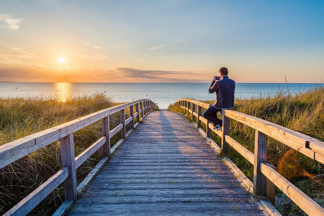 Weissenhäuser Strand, Ostholstein, Schleswig-Holstein, Germany, Man photographing the sunset on a pier to the Baltic Sea