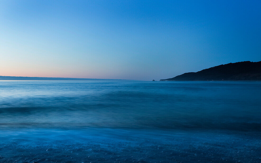 Seascape at sunset with clear, blue sky and tranquil ocean water, Karamea beach; South Island, New Zealand