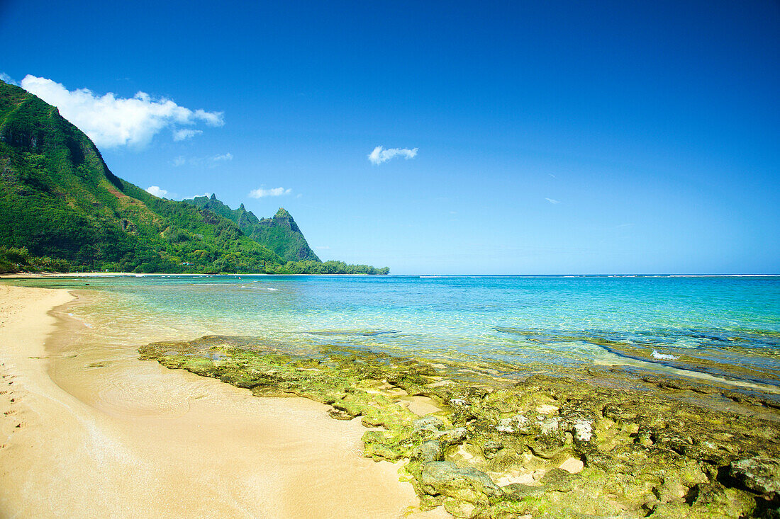 Clear turquoise ocean water and the rugged mountainous landscape on the island of Kauai; Kapaa, Kauai, Hawaii, United States of America